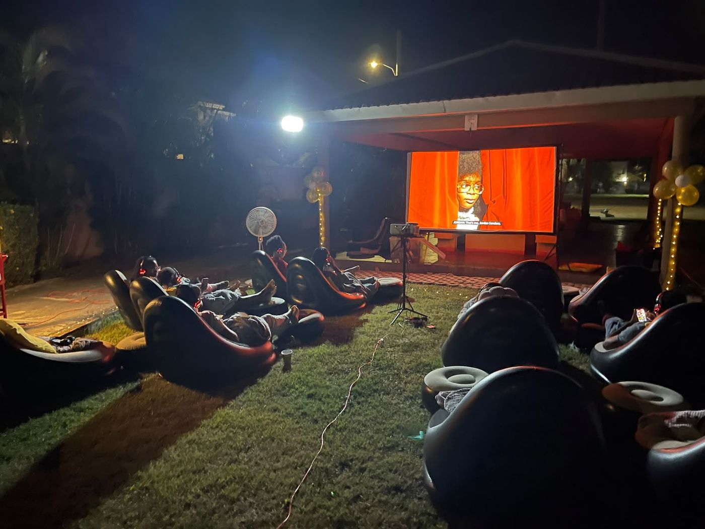Family watching a film at a private outdoor cinema in a Jamaican back yard at night